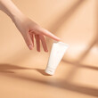 Woman's hand touches a mockup of white tube of cream. Unlabeled packaging for cosmetics in sunlight on beige background. Concept of skincare. Harsh shadows