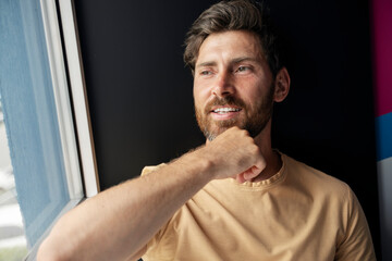 Closeup portrait of attractive happy bearded man looking away at home