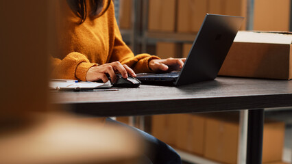 Wall Mural - Startup owner working on stock inventory with laptop, planning order distribution for business management in storage room. Worker doing supply chain shipment at desk, retail products. Handheld shot.