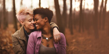 Mixed Lesbian Couple In Love, Girlfriends Hugging And Smiling In Nature At Sunset, Autumn Season. Romantic Scene Between Two Loving Women, Female Gay Tenderness.