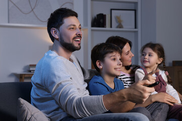 Wall Mural - Happy family watching TV at home in evening. Father changing channels with remote control