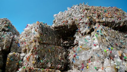 Wall Mural - Multiple stacks of compressed transparent plastic garbage at waste recycling factory in open air. Slow motion