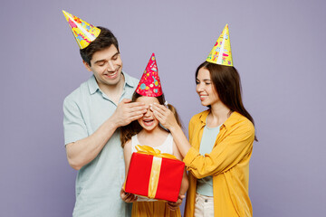 Wall Mural - Young parents mom dad with child kid daughter girl 6 years old wear yellow casual clothes cone cover eyes give present box with gift ribbon bow isolated on plain purple background. Family day concept.