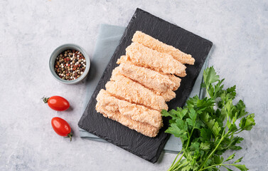 Fish fillet sticks, raw, not fried on a slate board with parsley on a light background with  tomato and spices. Diet and healthy food.