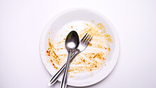 Cutlery sits on a white plate of finished food on a white table.