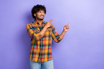 Photo of young man promoter student wear plaid shirt indicate fingers empty space looking advertisement isolated on purple color background