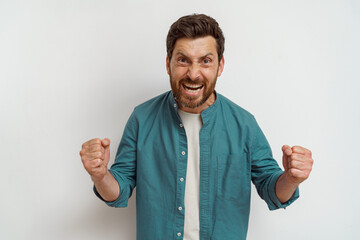 Wall Mural - Emotional smiling male fan is standing on white background and screaming with rise arms