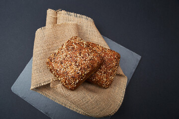 Two freshly baked rustic square shaped bread loaves with sesame seeds on the vintage rustic country style sackcloth grey stone plate and solid fond plain black background