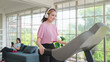 © M Stocker - Happy young asian women in sportswear wearing headphones while exercising on the machine at home. Young women training on elliptical machine. Health care concept