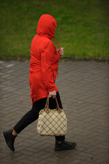 Wall Mural - a woman in rainy weather with a bright red jacket with a plaid bag in her hands with a hood on her head