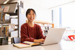 © Austockphoto - Young adult asian woman at the library studying and using her laptop