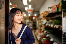 Young Adult Asian Woman Standing At The Door Of A Small Local Grocery Store