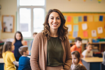 portrait of smiling teacher in a class at elementary school looking at camera with learning students