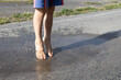 feet of a barefoot child who joyfully jumps in a transparent puddle on the pavement after rain. Changes in the weather in summer. close-up of the legs. Interesting fun childhood