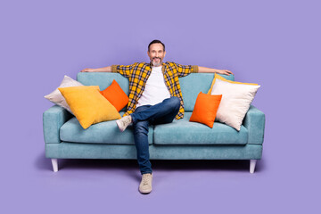 Wall Mural - Photo of cheerful man boss wear plaid stylish clothes sit soft comfort sofa enjoy break pause isolated over purple color background