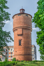 Trostyanets, Sumy Oblast, Ukraine - June 18, 2023: Round Red Brick Water Tower In Trostianets. Wild Pigeons Sit On The Roof Of A Tall Building Among The Summer Greenery, Vertical