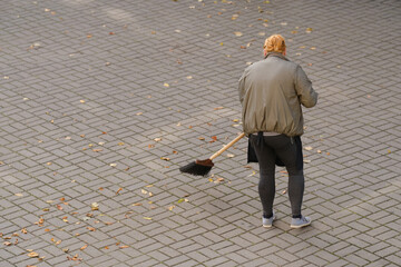 Wall Mural - woman street cleaner in gray clothes sweeps the street