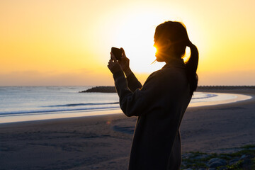 Sticker - Silhouette of woman use camera to take photo at sunset in the beach