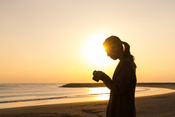 Poster - Silhouette of woman use camera to take photo at sunset in the beach