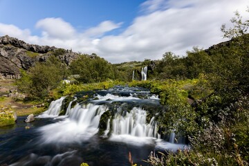 Sticker - Scenic waterfall cascading down a rocky terrain, surrounded by lush green vegetation in Gjain valley