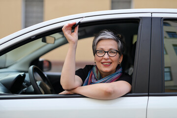 Sticker - A happy senior woman shows her independence and enjoyment in driving a new car. She is a retired businesswoman who loves traveling and smiling.