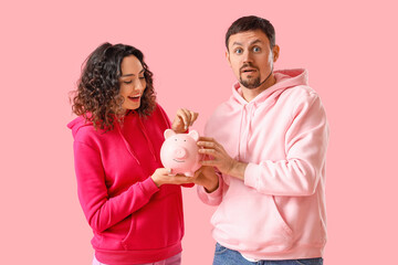 Wall Mural - Young couple with piggy bank on pink background