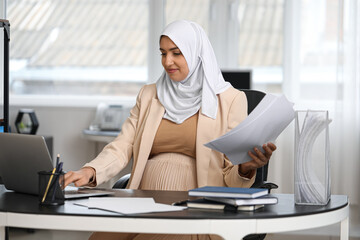 Poster - Young pregnant Muslim woman working with documents at table in office