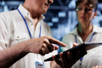 Poster - Teamworking colleagues using tablet to examine supercomputers for power fluctuations. Licensed engineers monitoring high tech server hub machines, identifying potential defects