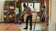 Interracial couple vacuuming floors and cleaning furniture on shelves, sweeping dust or dirt with tools. Life partners using vacuum cleaner with hose, gloves and rags to clean household. House chores.
