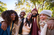 © CarlosBarquero - Group multi-ethnic friends posing laughing outdoor winter portrait. Young people hugging together look smiling at camera holiday photo in park on sunny day. Friendship relationships millennial.
