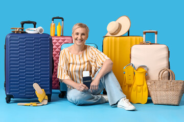 Poster - Mature woman with passport and suitcases sitting on blue background