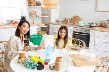 Wall Mural - Asian mother with her little daughter sorting garbage in kitchen