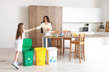 Wall Mural - Little girl with her mother sorting garbage in kitchen