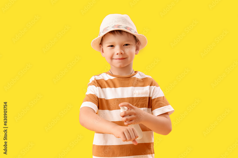 Little boy applying sunscreen cream on yellow background