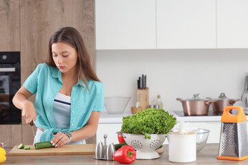 Young woman cutting cucumber for salad in kitchen