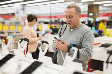 Wall Mural - Attentive European man chooses a mobile phone in an electronics store to buy it