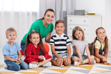 Wall Mural - Nursery teacher and group of cute little children on floor in kindergarten. Playtime activities