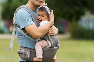 father consoling his crying infant in baby carrier in park