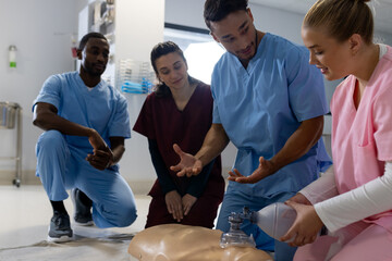 Biracial male doctor with diverse trainee doctors learning cpr on model at hospital