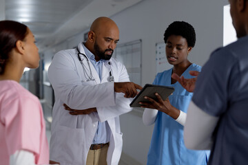 Wall Mural - Diverse doctors using tablet and discussing work in corridor at hospital