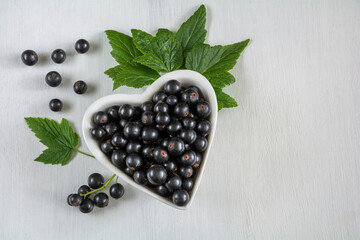 Wall Mural - Currant berries in a white heart-shaped bowl on a white wooden surface