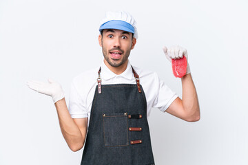 Butcher caucasian man wearing an apron and serving fresh cut meat over isolated white background with shocked facial expression