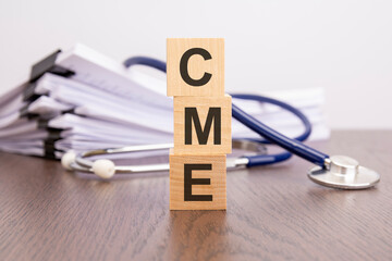 Wall Mural - text CME written on wooden cubes near a stethoscope on a paper background. CME - Continuing Medical Education, medical concept