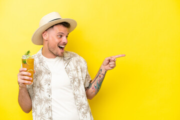 Poster - Young caucasian man holding a cocktail isolated on yellow background pointing finger to the side and presenting a product