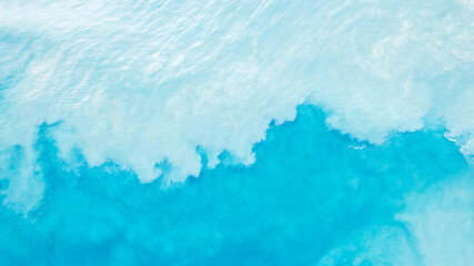 top view of light blue water with white sand. waves raise sand and a mix with turquoise water is obt