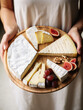 Woman holding a cheese plate with camembert, brie cheese, grapes and figs on wooden board, serving snack, food photography, top view photo