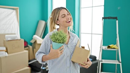 Wall Mural - Young blonde woman smiling confident holding package and plant at new home