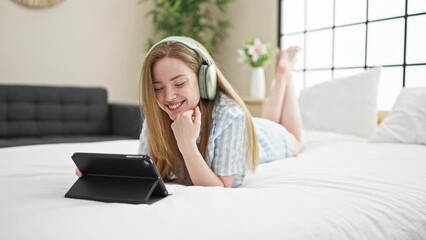 Poster - Young blonde woman watching video on touchpad lying on bed at bedroom