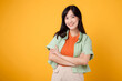 young 30s asian woman wearing orange shirt showing arm cross gesture on chest isolated on yellow background. Confident portrait and well being concept.