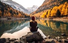 Beautiful woman in yellow sweater sitting on a rock and looking at the mountain lake.